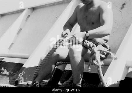 Das Foto wurde ungefähr 1961-09-22 aufgenommen. Ein Mann sitzt auf einem Schiff. Er teilt das Zugholz zusammen. African travel35 Bilder in Serie. Stockfoto