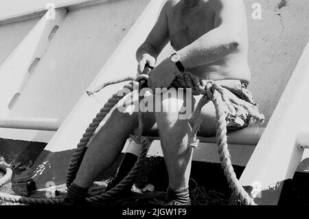 Das Foto wurde ungefähr 1961-09-22 aufgenommen. Ein Mann sitzt auf einem Schiff. Er teilt das Zugholz zusammen. African travel35 Bilder in Serie. Stockfoto