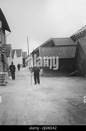 Ein älterer Mann mit einem Stock und einem Hut steht auf einer Straße in einer kleinen Küstengemeinde. Neben ihm ist ein Deal mit einem Schild: 'Specialies'. Hunnebostrand im Jahr 1936. Nach dem Buch Swedish West Coast Fishermen. 1949 von Olof Hasslöfjohan 'Stockebun' Samuelsson mit einem Stock in der Hand, Hunnebostrand 1936. Foto O. Hasslöf / Göteborg City Museum. Erschienen in Bohuslän in schwarz-weiß; Quirin, Bertil, S. 217. Glasplatte defekt. Stockfoto