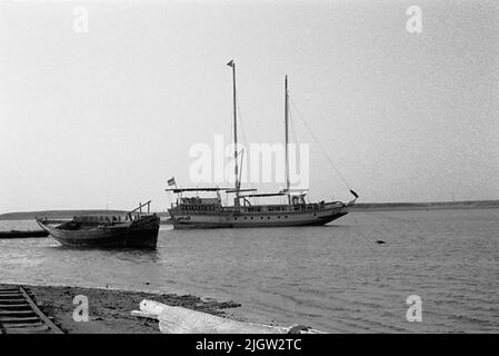 African trip, Port Sudden Acquisition: Bücher und Archivmaterial.36 Bilder in Serien. Das Foto wurde ungefähr 1961-08-22 aufgenommen. Ein Schiff ist in einer Meeresbucht verankert. Weiter in Richtung Strand ist ein abgenutztes Schiff auf dem Boden, nur der Rumpf ist intakt. Stockfoto