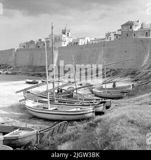 14. Schweden, Italien. Fotojournal ist bei B.M.A. erhältlich + Fotoalben. Erwerb: Bücher und Archivmaterial. Fotos aufgenommen 1959-10-28,12 Bilder in Serie. Nach Angaben: Italien. Adriaküste, Thermoli, 28/10 -59. Überdachte und unbedeckte Fischerboote mit lateinischen Rigs, die am Strand in Betrieb genommen wurden. An einem Strand befinden sich mehrere Boote. Dahinter befindet sich eine Gemeinde in einer Höhe, die Höhe ist mit einer Wand verstärkt, die entlang des Strandes verläuft. Stockfoto
