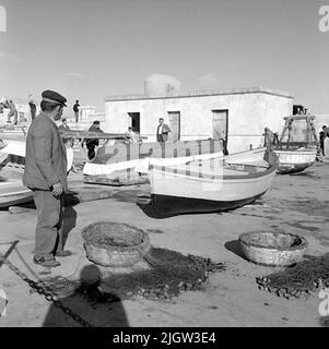 17. Italien. Fotojournal ist bei B.M.A. erhältlich + Fotoalben. Erwerb: Bücher und Archivmaterial. Fotos aufgenommen zwischen 1959-10-28 und 1959-10-29,12 Bilder in Serie. Nach Angaben: Italien. Adriaküste, Bari, 29/10 -59. Kleine Boote verschiedener Typen. Mehrere Boote befinden sich auf einem Plan in einem Hafen. Im Vordergrund steht ein Mann, der seine Netze in der Sonne wischt. Die Netze befinden sich in Korbkörben. Stockfoto