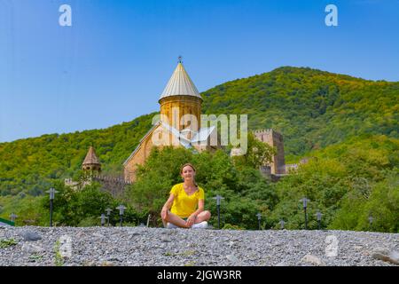 Ein Mädchen in Gelb sitzt am Ufer in der Nähe der Festung Ananuriv in Georgien Stockfoto