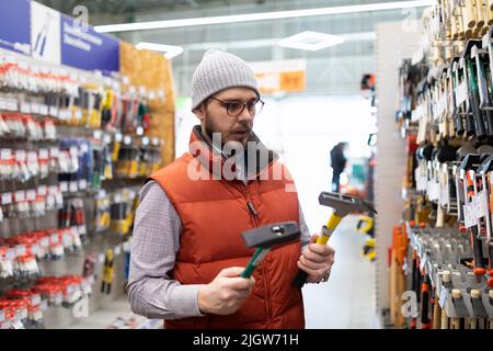 Ein Mann wählt einen neuen Hammer in einem Baumarkt Stockfoto