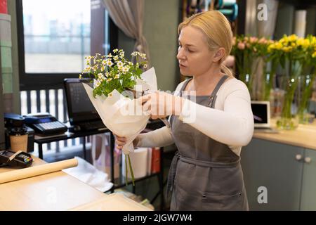 Blumengeschäft Manager entfernt überschüssige Blätter auf einem Strauß mit Gartenscheren Stockfoto
