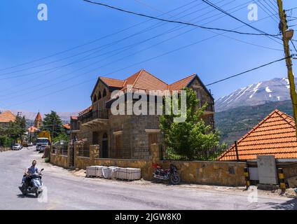 Mann auf einem Motorroller, der vor einem alten libanesischen Haus vorbeifährt, North Governorate, Bsharri, Libanon Stockfoto