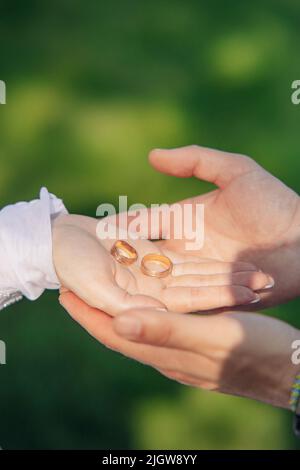 Hände des Bräutigams halten Hand der Braut mit goldenen Ringen auf ihrer Handfläche. Nahaufnahme. Stockfoto