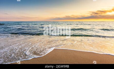 Sandstrand bei Sonnenaufgang. Schöner Meereshintergrund. Ruhige Wellen waschen das Ufer. Wolken glühen im Morgenlicht. Sommerurlaub und entspannende Erholung Stockfoto