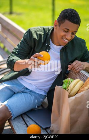 Kerl, der in die Tüte mit Essen auf der Bank sitzt Stockfoto