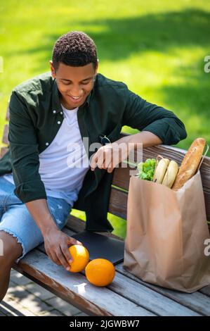 Kerl, der Orangen ansieht, die auf der Bank sitzen Stockfoto