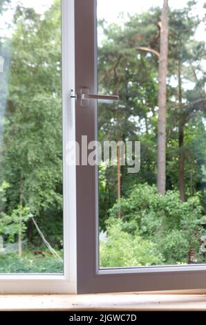 Plastikfenster im Haus mit Blick auf den Pinienwald. Ein sonniger Sommertag Stockfoto