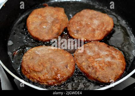 Fleischburger, die auf flachem Öl auf einer Bratpfanne gebraten werden, Hackfleischpastete in Form von Hackfleisch, und es ist ein beliebter schneller Schrott Stockfoto