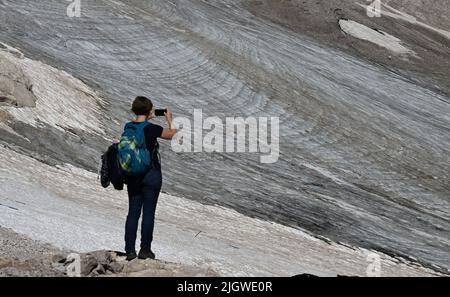 Grainau, Deutschland. 13.. Juli 2022. Ein Wanderer fotografiert die Überreste des nördlichen Schneefernergletschers auf dem Zugspitzplatt. Die warmen Temperaturen beeinflussten in diesem Sommer die Reste des Gletschers auf der Zugspitze. Quelle: Angelika Warmuth/dpa/Alamy Live News Stockfoto