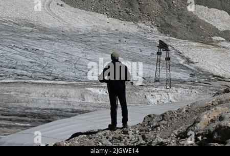 Grainau, Deutschland. 13.. Juli 2022. Ein Wanderer schaut auf die Überreste des nördlichen Schneefernergletschers auf dem Zugspitzplatt. Die warmen Temperaturen beeinflussten in diesem Sommer die Reste des Gletschers auf der Zugspitze. Quelle: Angelika Warmuth/dpa/Alamy Live News Stockfoto