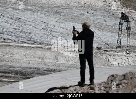 Grainau, Deutschland. 13.. Juli 2022. Ein Wanderer fotografiert die Überreste des nördlichen Schneefernergletschers auf dem Zugspitzplatt. Die warmen Temperaturen beeinflussten in diesem Sommer die Reste des Gletschers auf der Zugspitze. Quelle: Angelika Warmuth/dpa/Alamy Live News Stockfoto