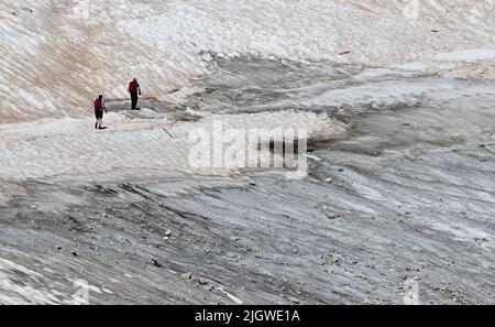 Grainau, Deutschland. 13.. Juli 2022. Wandern auf dem Zugspitzplatt über Schneereste am nördlichen Schneeferner Gletscher. Die warmen Temperaturen beeinflussten in diesem Sommer den Gletscherrest auf der Zugspitze. Quelle: Angelika Warmuth/dpa/Alamy Live News Stockfoto