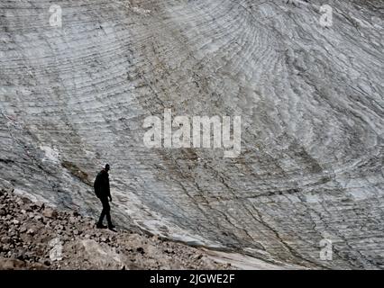 Grainau, Deutschland. 13.. Juli 2022. Ein Urlauber steht auf dem Zugspitzplatt vor dem nördlichen Schneefernergletscher. Die warmen Temperaturen beeinflussten in diesem Sommer den Gletscherrest auf der Zugspitze. Quelle: Angelika Warmuth/dpa/Alamy Live News Stockfoto