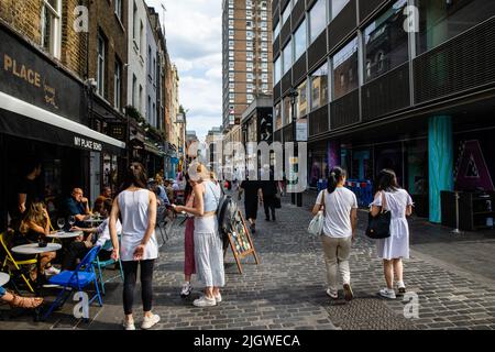 London, Großbritannien. 11.. Juli 2022. In der Berwick Street in Soho sitzen Menschen vor den Restaurants. Berwick Street hat in den letzten zehn Jahren große Umbaumaßnahmen erlebt, Stockfoto