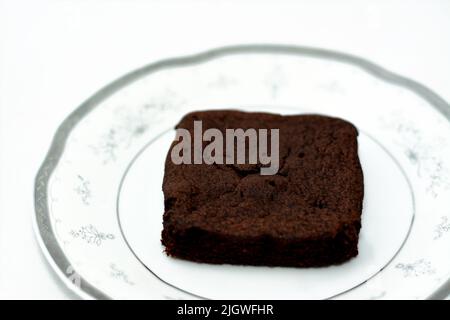 Süße Brownie Schokoladenkuchen Stück mit Kakaopulver auf einem weißen Teller isoliert auf einem weißen Hintergrund, Brownies in der Regel mit Kaffee serviert, süß Stockfoto