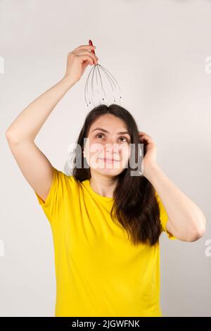Eine Frau mit einem flexiblen Massagegerät aus Metall zur Selbstmassage des Kopfes auf weißem Hintergrund. Stockfoto