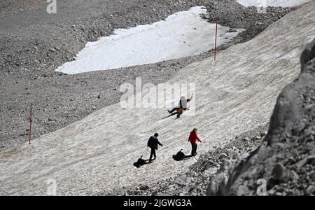 Grainau, Deutschland. 13.. Juli 2022. Urlauber schlitten über einen Schneerich auf der Zugspitzplatte. Die warmen Temperaturen belasten in diesem Sommer den Restgletscher des Nördlichen Schneeferners auf der Zugspitze. Quelle: Angelika Warmuth/dpa/Alamy Live News Stockfoto