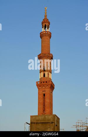 Ein hohes Minarett mit goldenem Ornament einer Moschee, die im Bau ist, Minarett oder Turm, der nach Himmel, islamischer Religion und Architektur strebt Stockfoto