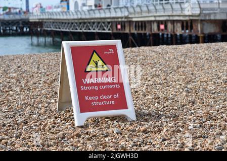 Rotes Warnschild an einem Strand, Warnung vor der Gefahr von hohen Strömungen um einen Pier herum. Stockfoto