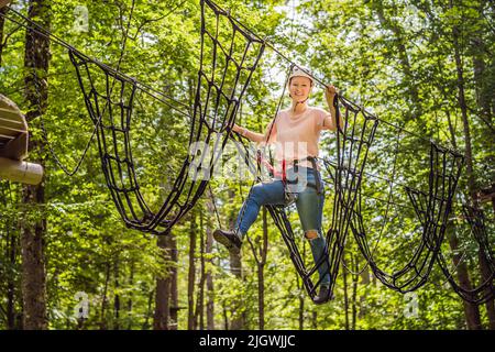 Glückliche Frauen Mädchen weiblich Gleiten Klettern in extremen Straße Trolley Zipline im Wald auf Karabiner Sicherheitslink auf Baum zu Baum top Seil Abenteuerpark Stockfoto