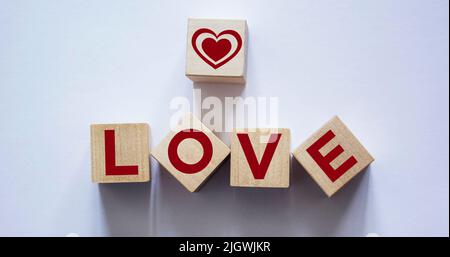 Wortliebe aus Holzbuchstaben in der Nähe von roten dekorativen Herzen auf Holzwürfel und hellem Hintergrund Stockfoto