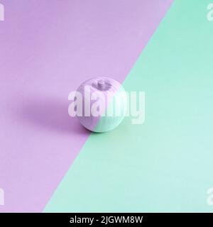 Mehrfarbiger Holzapfel auf violettem und grünem Hintergrund. Minimales abstraktes Konzept. Isometrisches quadratisches Layout mit Kopierbereich Stockfoto