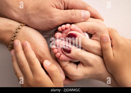 Die Beine des Neugeborenen befinden sich in den Händen des Vaters der Mutter und des älteren Bruders und der Schwester.Happy Family Concept. Stockfoto