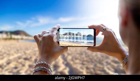 Frau am Strand von CoCoCoCoCoCoCoCoab, die mit ihrem Mobiltelefon ein Foto gemacht hat. Fotografieren mit einer Kamera eines Smartphones in Rio de Janeiro, Brasilien. Stockfoto