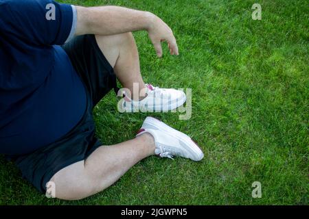 Der Bauch eines fetten, übergewichtigen Mannes ist mit Diabetes in der Nähe und bei Krankheit im Freien auf einem Rasen sitzend Stockfoto