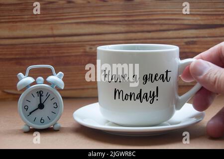 Begrüßungskonzept am Morgen - am Montag gibt es einen tollen Text auf einer Kaffeetasse mit Wecker auf einem Holztisch. Konzeptionell Stockfoto