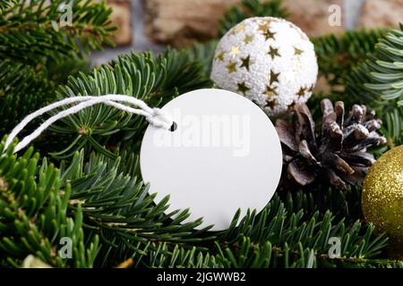 Weihnachtliche runde weiße Tag-Mockup mit weißer Kordel, Nahaufnahme auf natürlichem Tannenzweig, mit Zapfen und Weihnachtsdekoration, Weihnachtsverkauf-Konzept. Bl Stockfoto