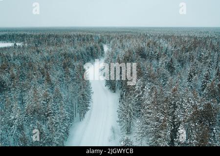 Luftdrohnenaufnahme einer leeren verschneiten Winterstraße im Wald Stockfoto