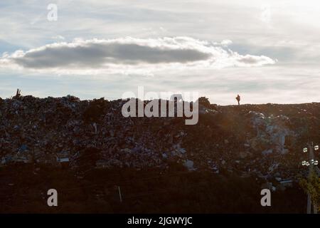 Blick auf die Müllkippe am Abend. Ein Arbeiter steht auf einem Berg von Müll. Stockfoto