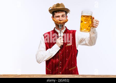 Fröhlicher Mann im traditionellen bayerischen oder deutschen Festkostüm mit großem Bierglas und gebratener Wurst zum Oktoberfest. Party, Urlaub, Werbung, Verkauf Stockfoto