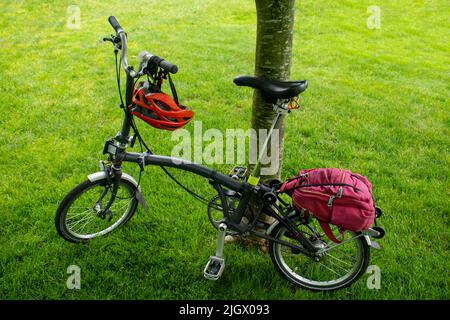 Componentry Fahrrad mit Titan-Heckrahmen und Gabel leichtes Faltrad auf einem Baum mit Helm und Rucksack lehnt Stockfoto