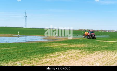 Eine kahle Stelle auf einem Feld mit Feldfrüchten. Nahrungsmittelkrise als Folge des Klimawandels. Ein Traktor besprüht ein Feld mit Herbiziden und mineralischen Ferti Stockfoto