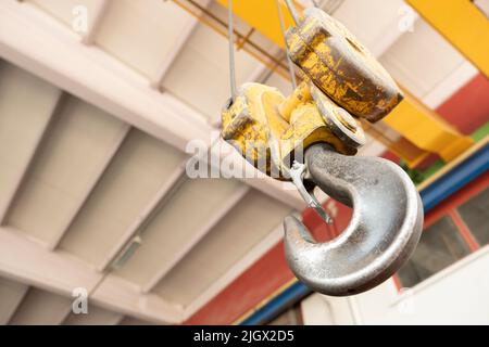 Kranhaken, Nahaufnahme Kranhaken für Laufkran im Werk. Bodenansicht oder gebrauchter und verfärbter gelber Haken mit Werkbetondecke. Stockfoto