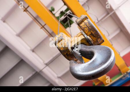 Alter Kranhaken, Ansicht von unten im Werk. Industrieller gelber alter Kranhaken, der von der Betondecke hängt. Konzeptfoto des Hebens schwerer Lasten. Stockfoto