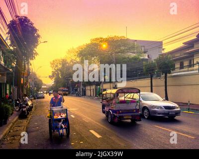 Fast eine leere 4-spurige Straße mit einem Auto, Tuk Tuk und Street Food Warenkorb während einer hellen gelben Himmel Sonnenuntergang. Stockfoto