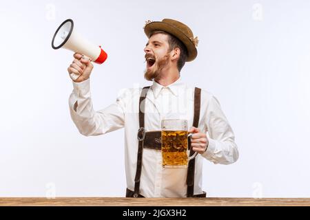 Staunender Mann in traditioneller bayerischer oder deutscher Festkleidung mit großem Bierglas, der beim Megaphon über den Oktoberfest-Start schreit. Party, Urlaub Stockfoto