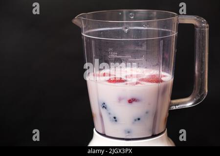 Milchshake in einer Schüssel mit einem Mixer aus Milch, Erdbeeren und Brombeeren auf schwarzem Hintergrund, ein Ort für Text Stockfoto