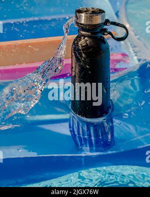 Eine schwarze isolierte Flasche auf einer Luftmatratze, auf die ein Wasserstrahl trifft Stockfoto