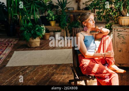 Junge wunderschöne Frau, die auf einem Stuhl neben dem Fenster sitzt Stockfoto