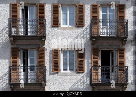 Schmiedeeisernes Balkongeländer mit Holzladertüren und Fenstern in gerenderter Außenfassade im Nachmittagssonnenlicht, das Schatten auf die Wand in CH wirft Stockfoto