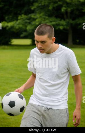 Ein neunzehnjähriger Jugendlicher, der in Einem öffentlichen Park Fußball spielt Stockfoto