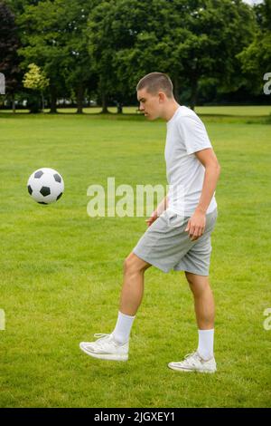 Ein neunzehnjähriger Jugendlicher, der in Einem öffentlichen Park Fußball spielt Stockfoto